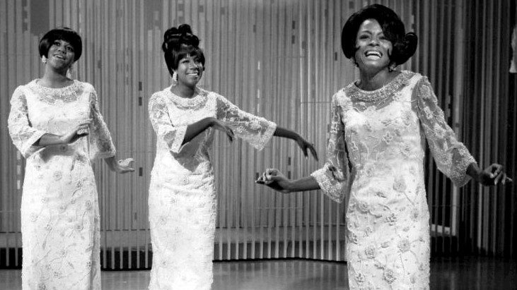 Florence Ballard, Mary Wilson, and Diana Ross wear matching sequined gowns and smile wide during a performance