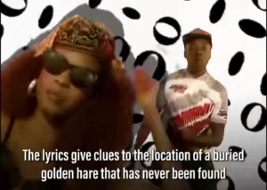 The image is from the "Pump Up the Jam" music video. A man and woman stand in front of a greenscreen. Text in an overlay reads, "The lyrics give clues to the location of a buried golden hare that has never been found." 